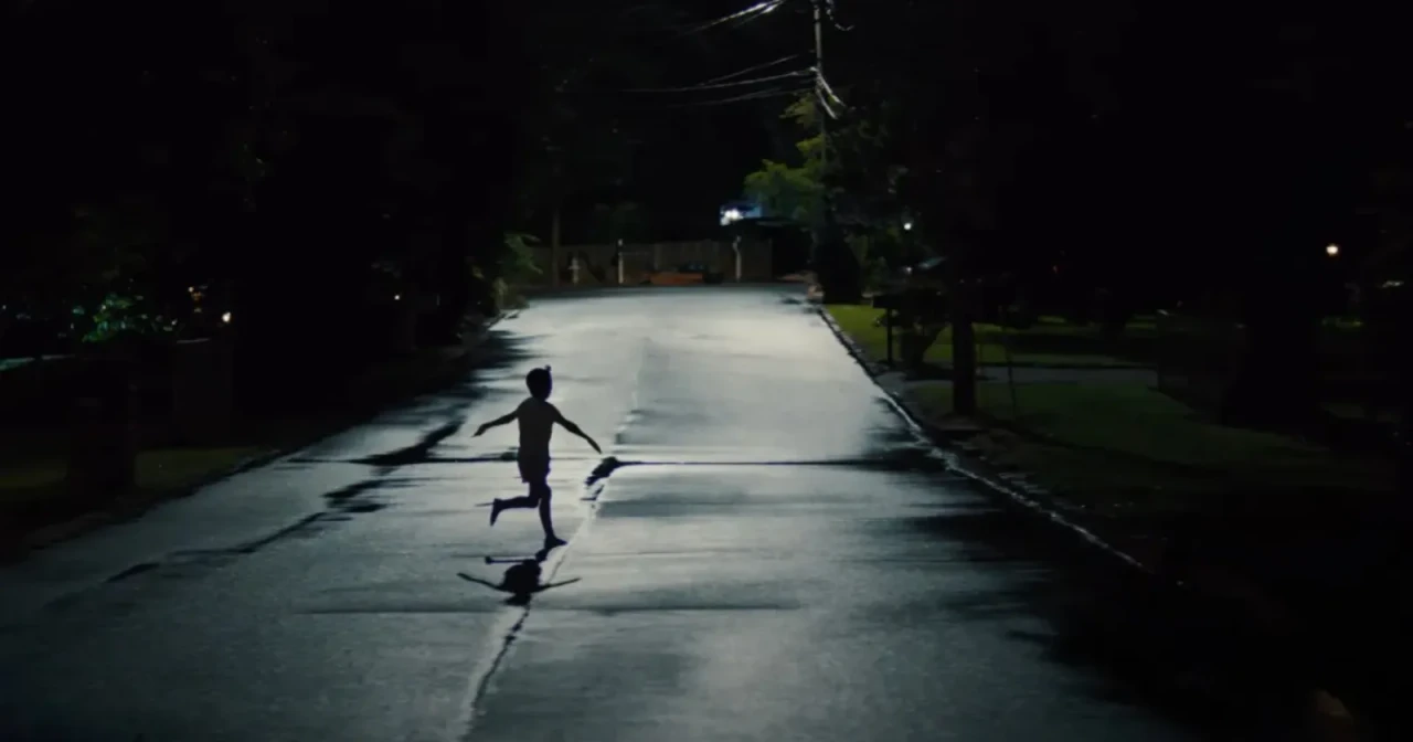 A screenshot from the 2025 horror film Weapons showing the silhouette of a child running down an empty street in the middle of the night with his arms stretched out by his sides.