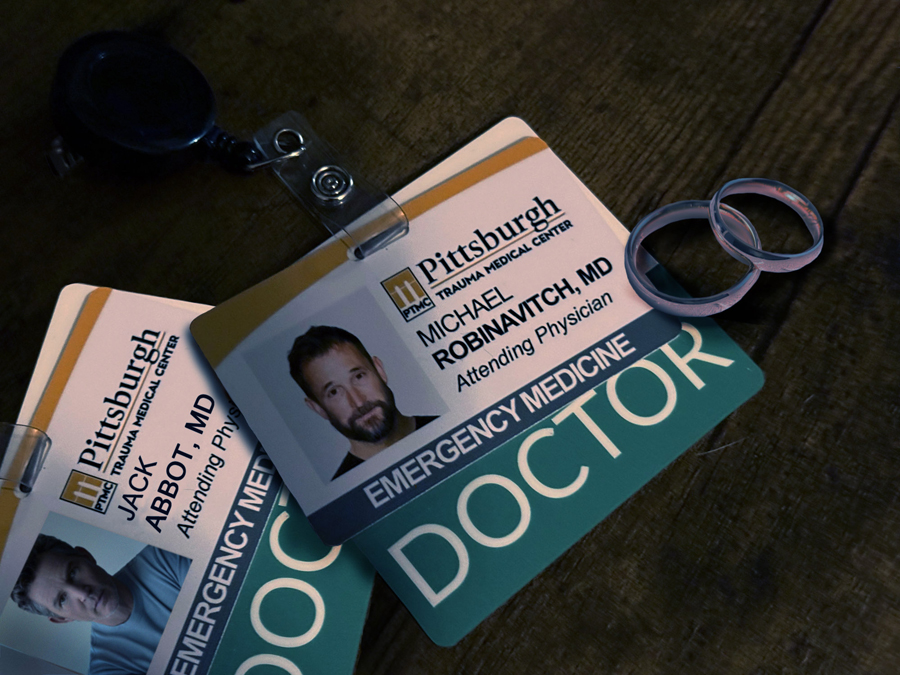 A photo of both Jack and Robby's hospital ID badges on a wood table with two wedding rings sat next to them
