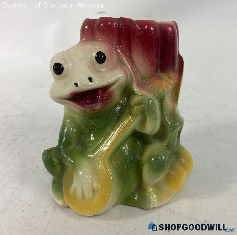 a product photo of a painted ceramic frog playing a banjo. its body is green, its banjo is yellow, and its face is pale white with smears of red around its mouth.