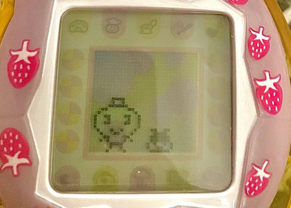 close up photograph of a tamagotchi connection device. on the screen is a memetchi and her baby