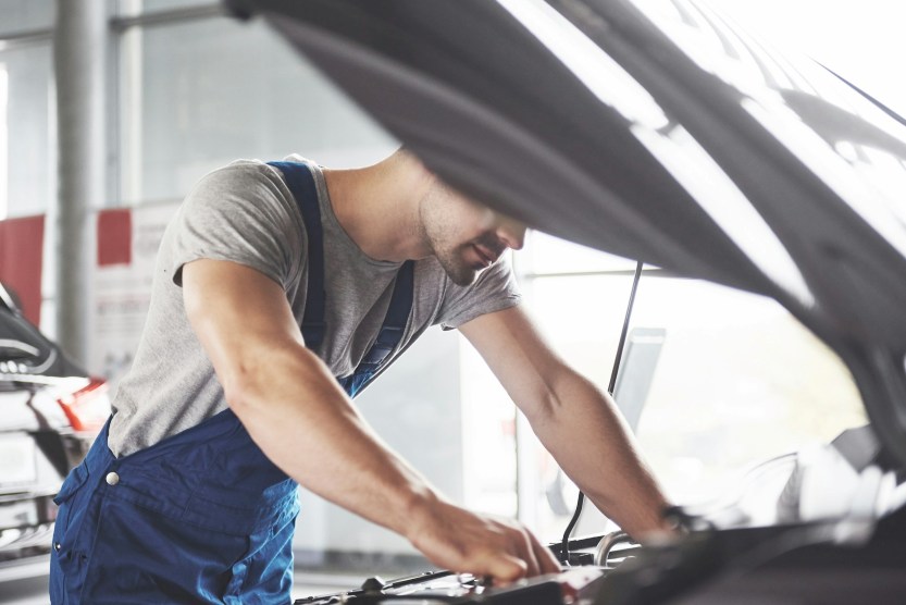 mechanic performing a pre-purchase vehicle inspection under the hood