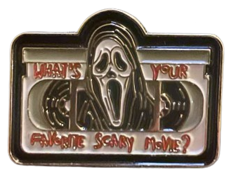 an enamel pin of ghostface from scream coming out of the audio hub of a cassette, with the words 'what's your favorite scary movie?' on the top & bottom part of the cassette