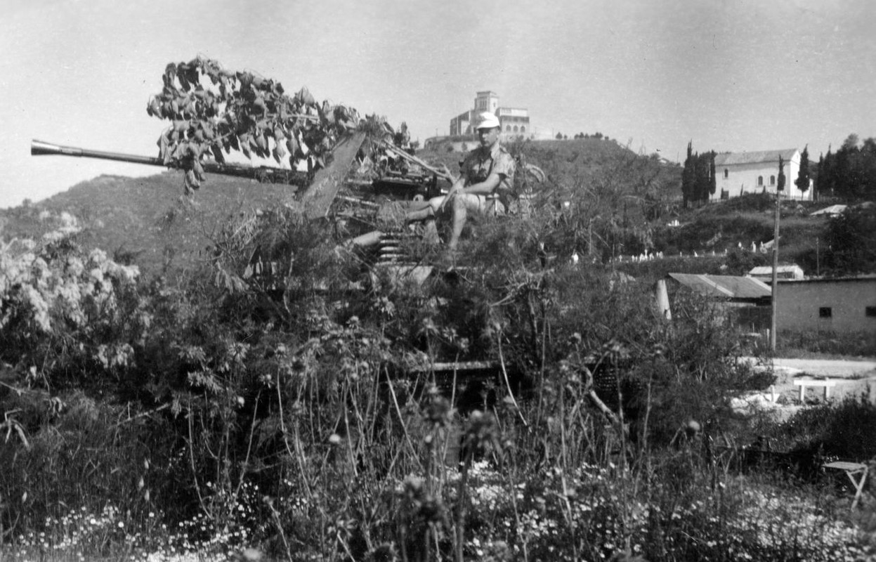 Ein Mann sitzt auf einem Geschütz, das mit Ästen und Blättern be