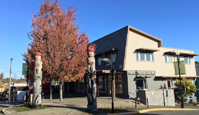 A building stands beside a tree featuring a colorful totem pole, showcasing a blend of nature and cultural art.