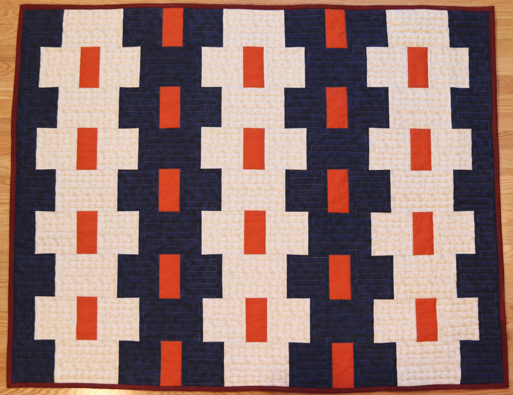 a navy-blue and cream-colored quilt with orange rectangles set in each of the primary colors in a repeating pattern