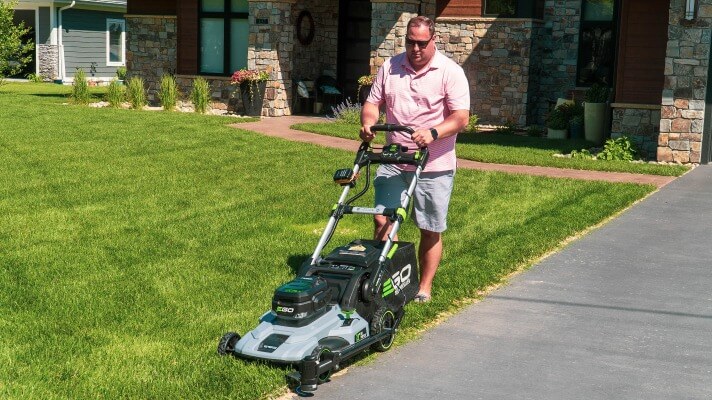 A man mowing the grass with a push lawn mower and Trimyxs attached