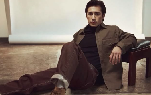 Shane Hollander sits on floor in brown pants and jacket