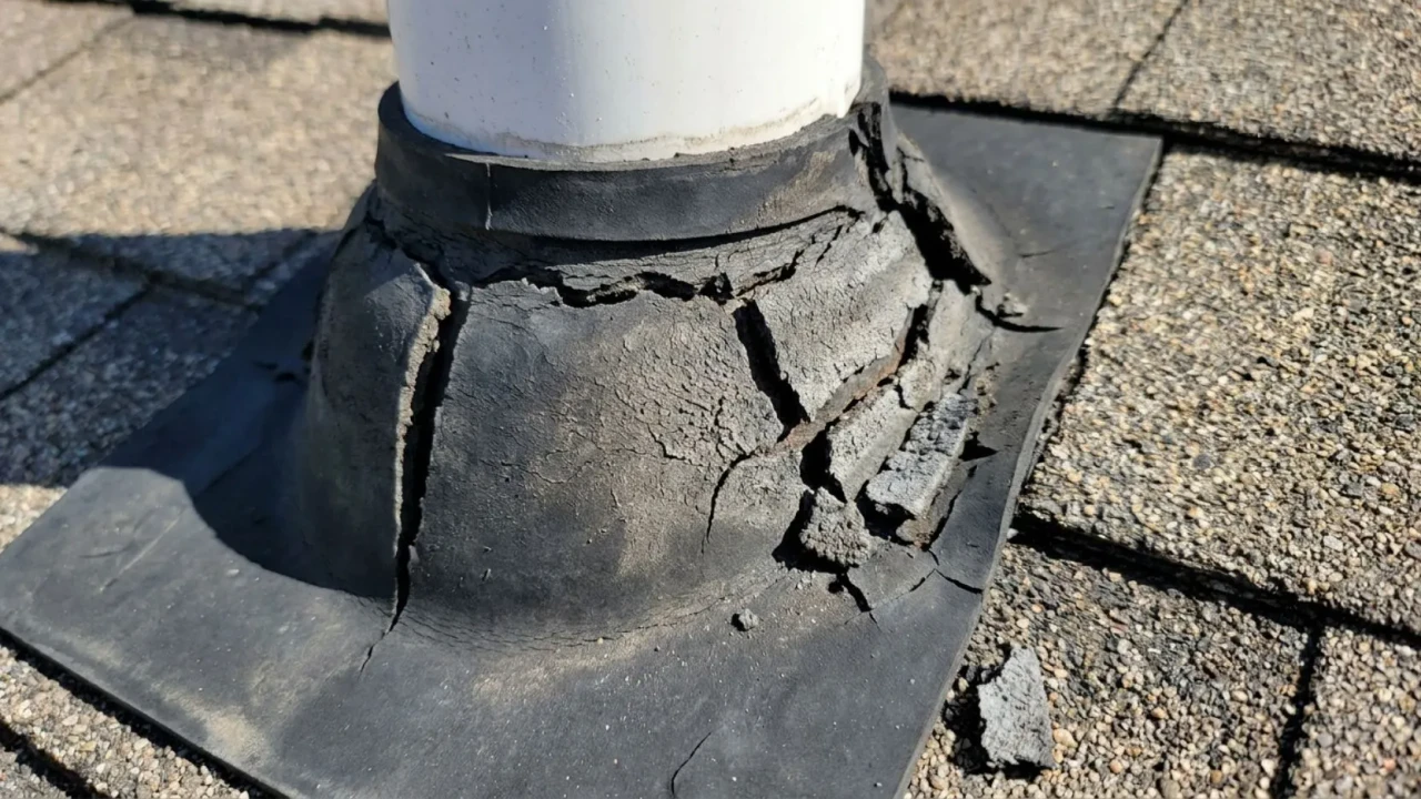 Cracked and deteriorated rubber pipe boot around a plumbing vent pipe on a residential asphalt shingle roof