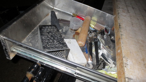A closeup of one of the kitchen counter drawers open. It's full of old dirty misc kitchen utensils.