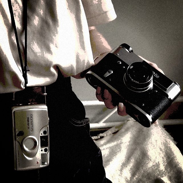 gros plan sur une main qui tient un appareil photo, un second appareil apparaît en fond, pendant en collier autour du cou d&#39;une silhouette