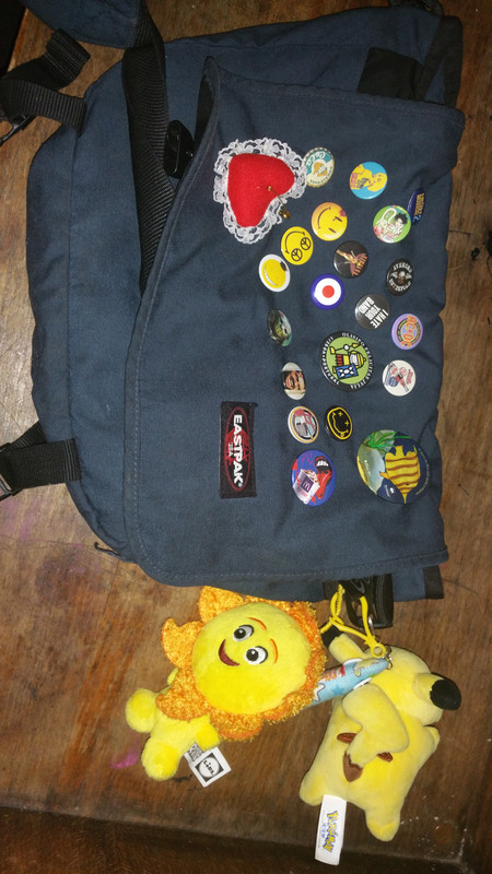 A messenger bag. It is bedazzled with various pins and has plushes attached.