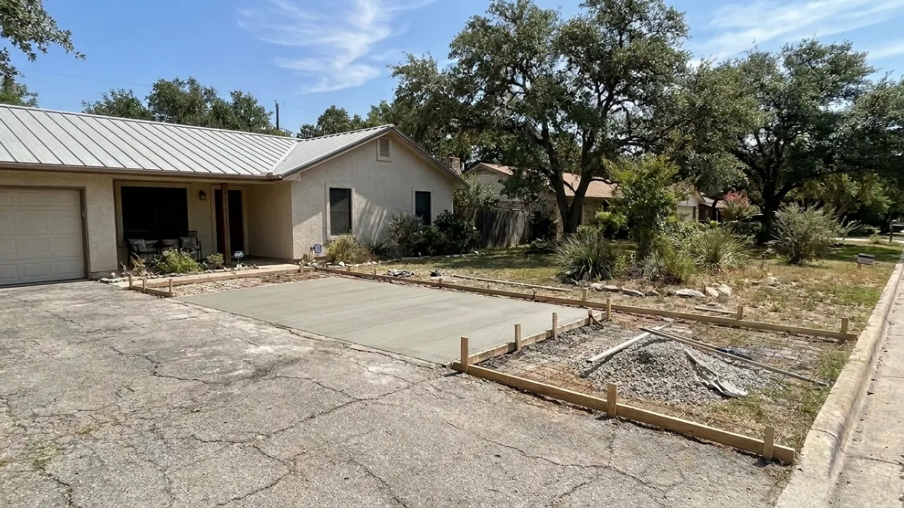 Newly poured broom-finish concrete parking pad beside a residential driveway in San Antonio TX with clean edges and proper drainage slope