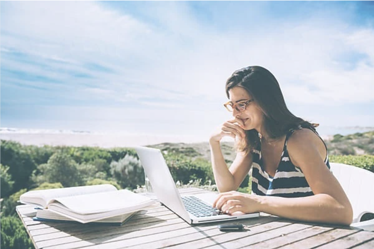 Woman working on a laptop at a scenic outdoor table.