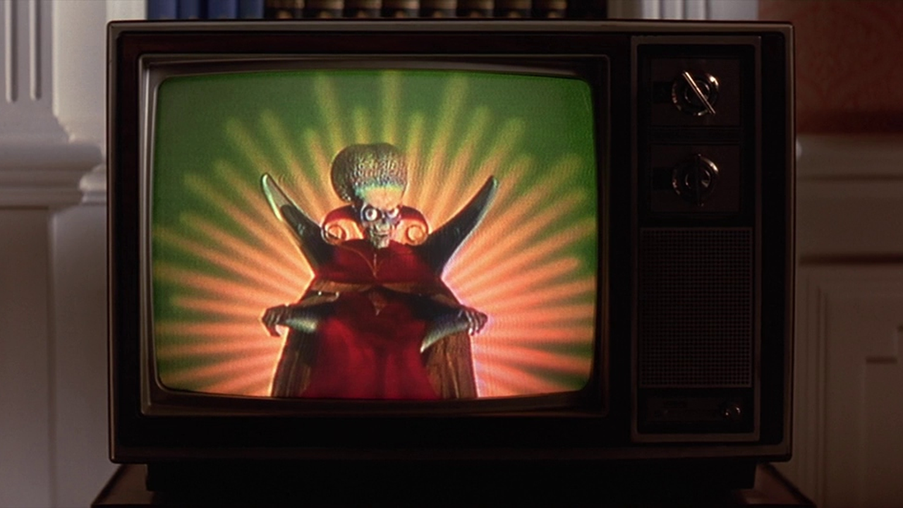 screencap do filme mostrando um marciano fazendo um pronunciamento em uma televisão vintage