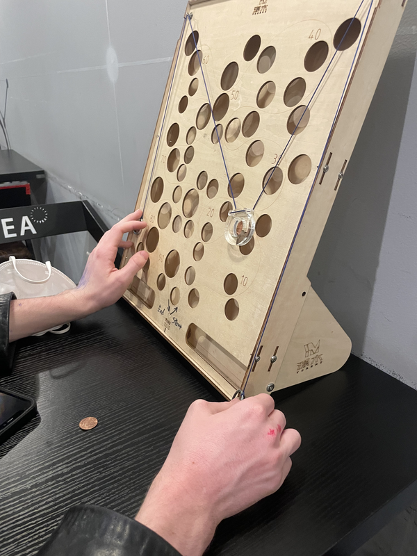 A photo of a game where you have a little holder attached to two strings and a coin on it. As you move the strings, you have to manuever around different holes in the board behind the coin so that the coin doesn't fall in. The photo is just of the board and my girlfriend's hands as she plays