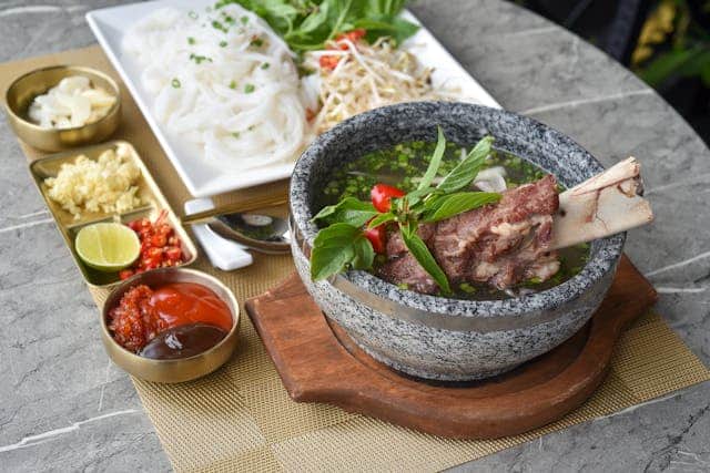 A bowl of bone broth with condiments on the side