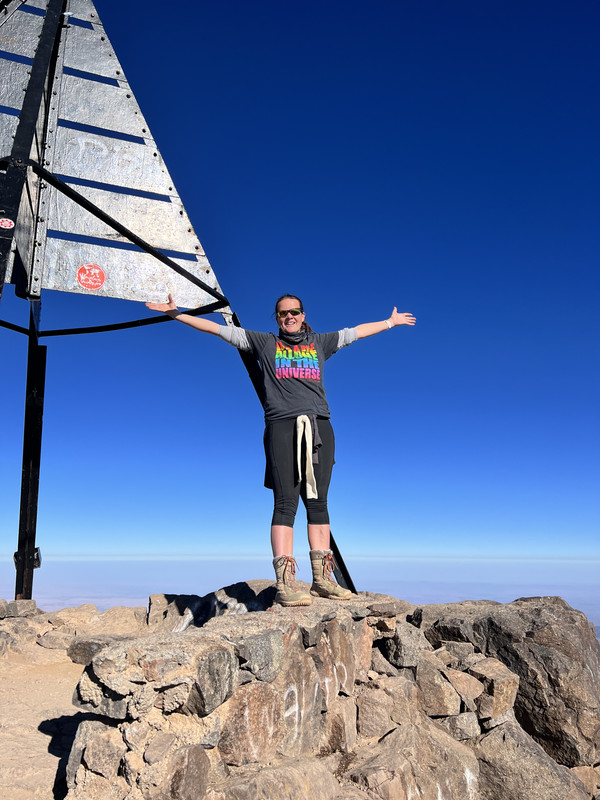 Gin, arms out, on a mountain peak