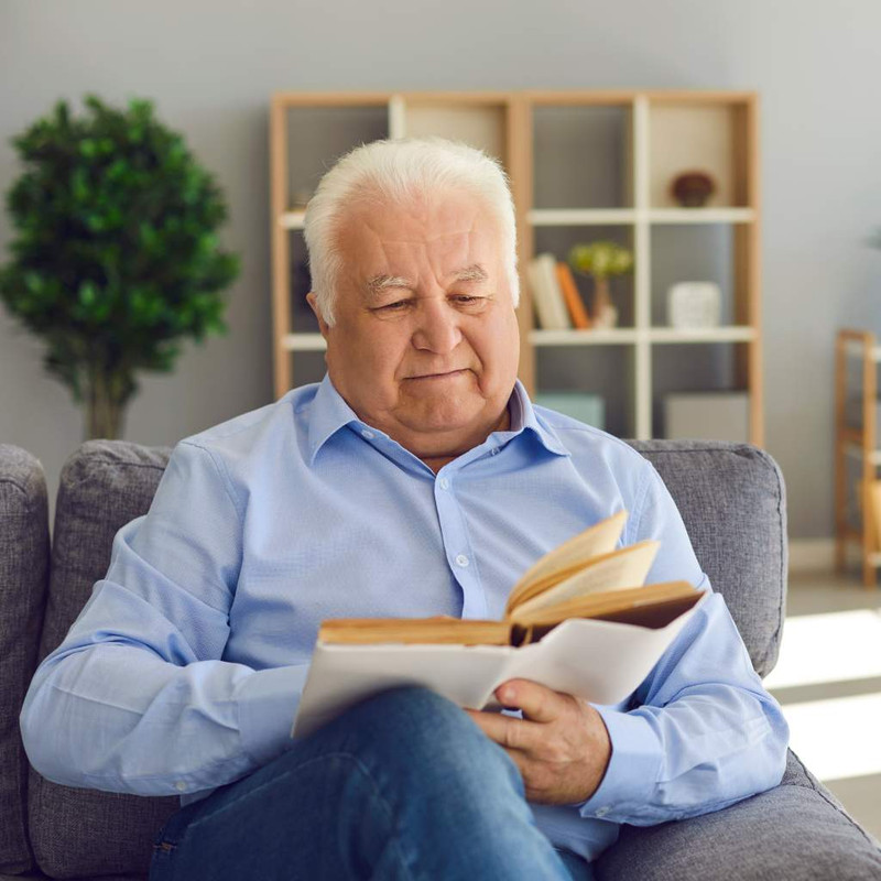 Happy-Retired-Man-Spending-Leisure-at-Home-and-Reading-Old-Book-Sitting-on-Couch-in-the-Living-Room