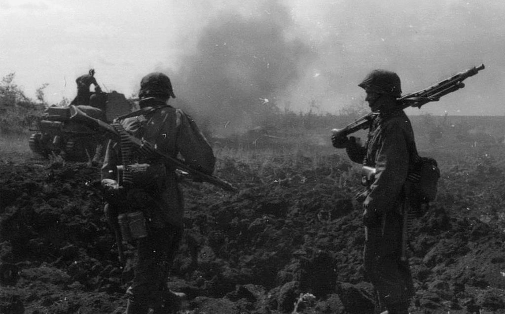 Tropas de asalto de las Waffen SS durante un breve descanso. Frente a ellos un cañón antitanque avanza por terreno quemado