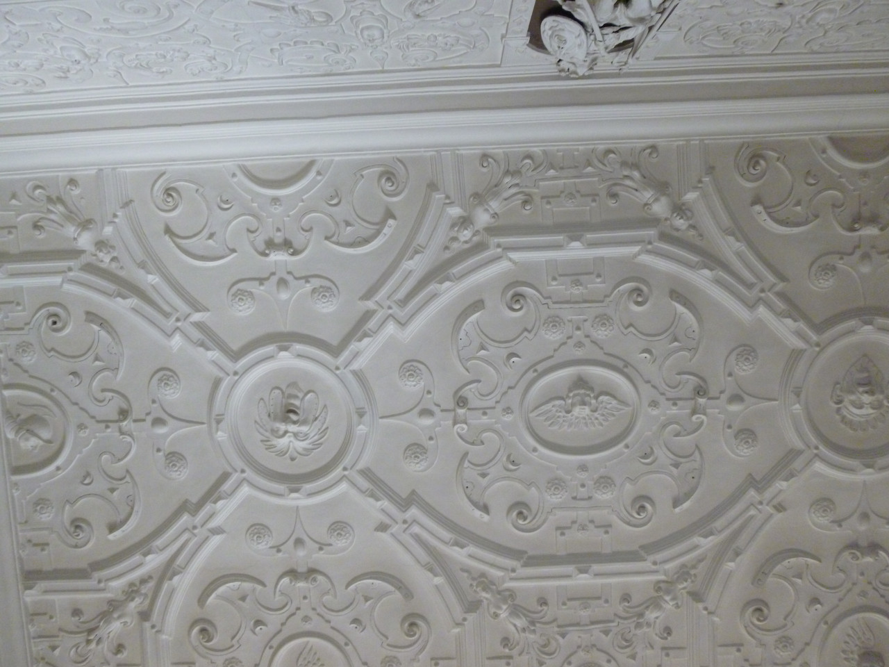 Photo of a stucco or stucco-style ceiling.  There are putti in the centre of circles, joined by hexagons which also have putti in the middle.