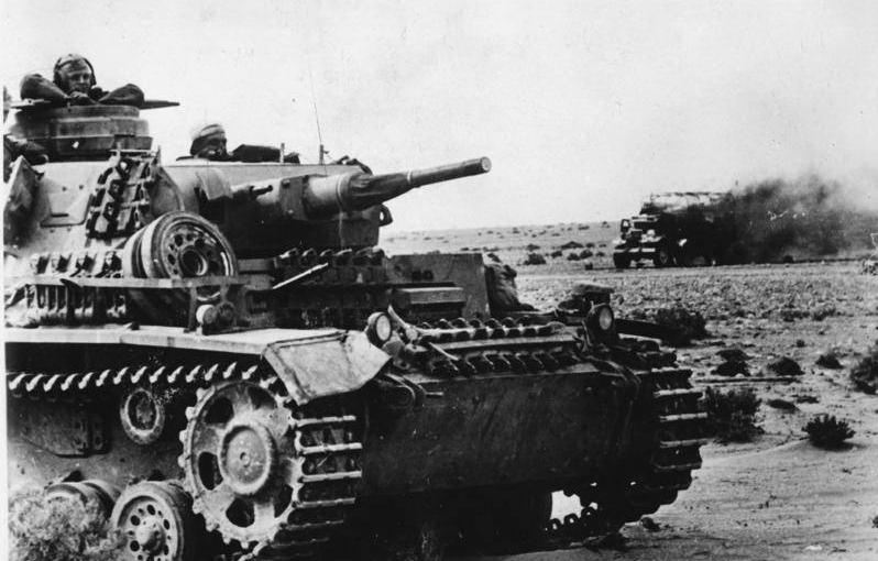 Un Panzer III del Afrika Korps pasando cerca de los restos de un vehículo en llamas británico