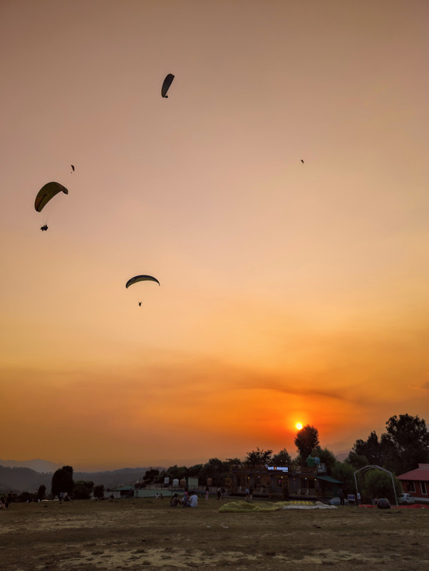 Tandem paragliders under an orange-and-blue sky on landing site at Bir