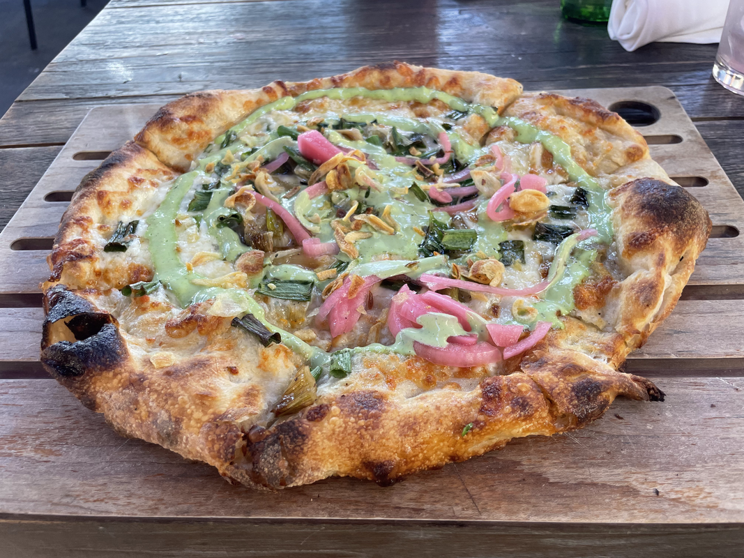 a photo of a pizza with red onions, crispy garlic, shallots, spring onions, and some kind of green ranch sauce on top.