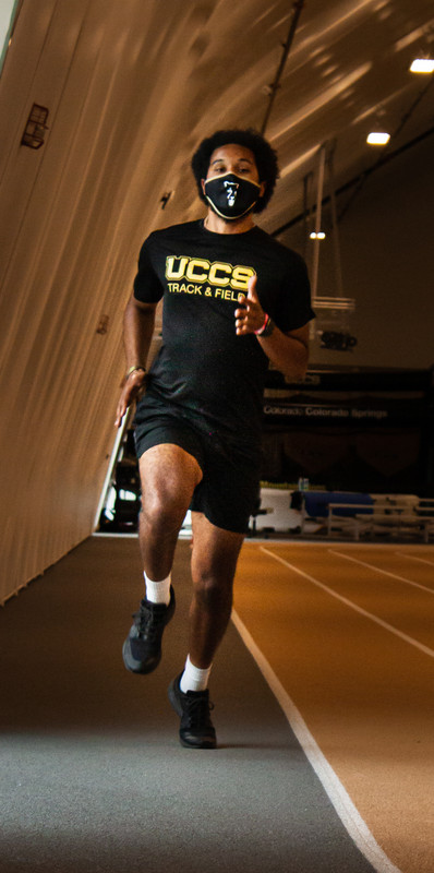 An athlete running on a track while wearing a mask. 