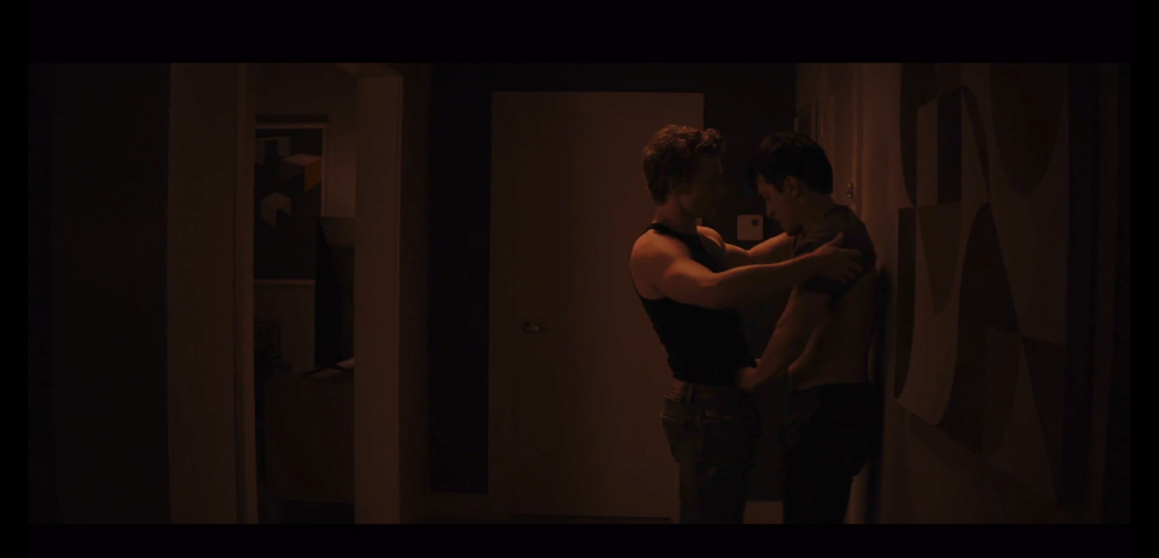 ilya is trying to pull shane's t-shirt off while shane tries to undo ilya's belt. ilya is in a black tank top and gray pants. shane is in a gray t-shirt that ilya has pulled up to his armpits and black pants.