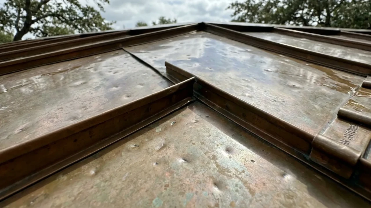 Close-up of copper standing seam panel showing cosmetic hail denting after a San Antonio storm event, with the seams and waterproofing fully intact