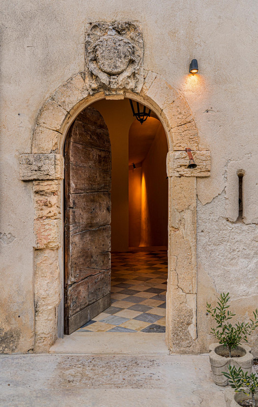 Historischer Steineingang von Château Bénat mit zurückhaltender Außenbeleuchtung, warmem Innenlicht und bewahrtem architektonischem Charakter