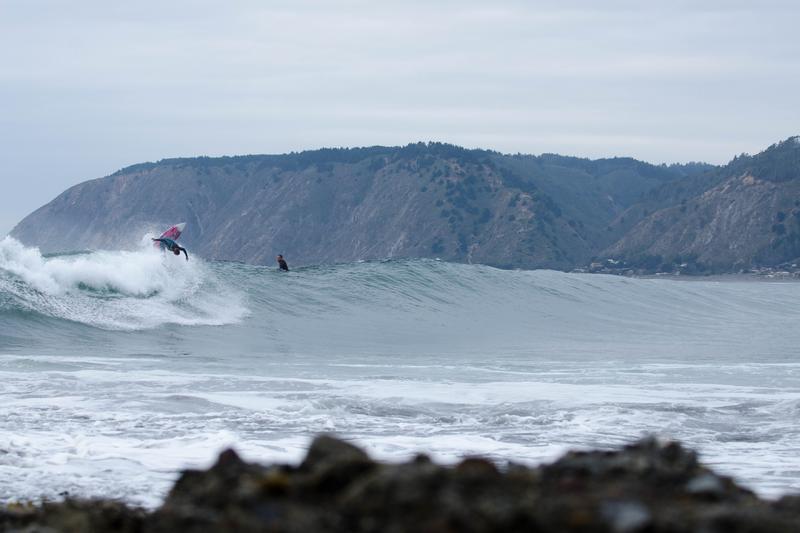 Surfista sobre una ola frente a los cerros de la costa de Litueche