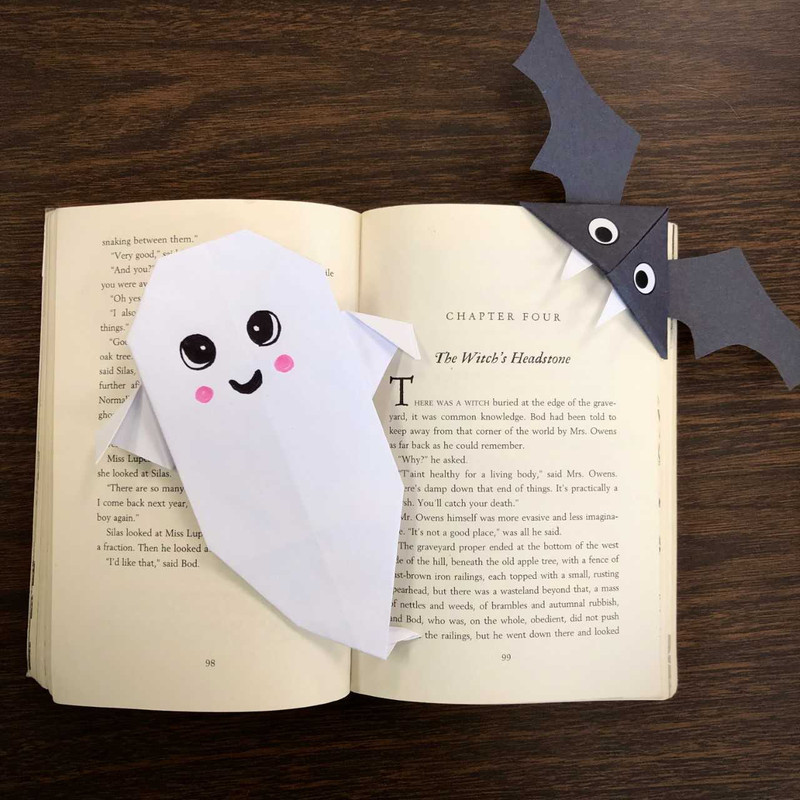 an open book with a paper bat bookmark and an origami ghost