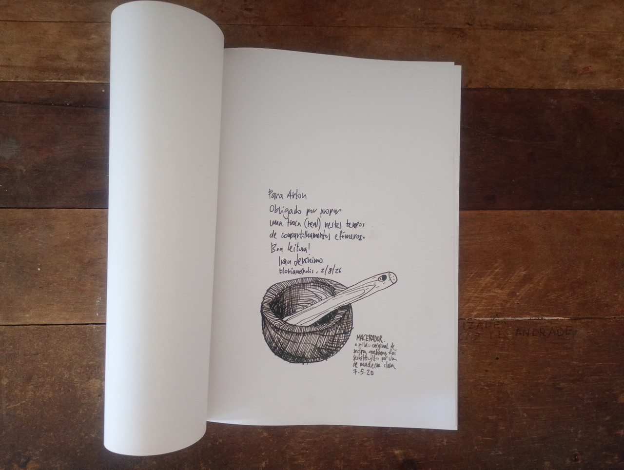 Imagem. O mesmo livro, só que aberto em sua contracapa, onde se vê um macerador com um pilão de pedra desenhado. Sobre isso lê-se 'Para Arlon, Obrigado por propor uma troca ― real ― nestes tempos de compartilhamentos efêmeros. Boa leitura! Ivan Jerônimo. Florianópolis, 2/8/26