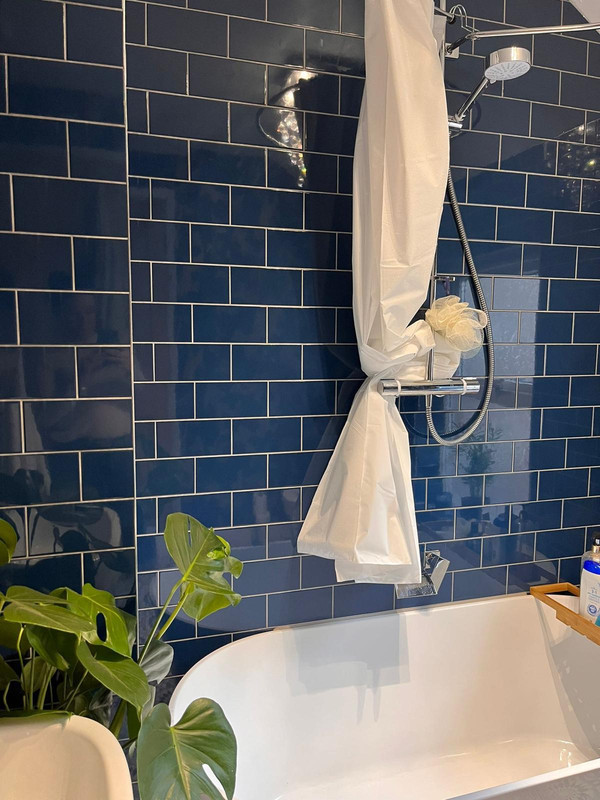 Elegant navy tiled bathroom with white bath and chrome shower fitting