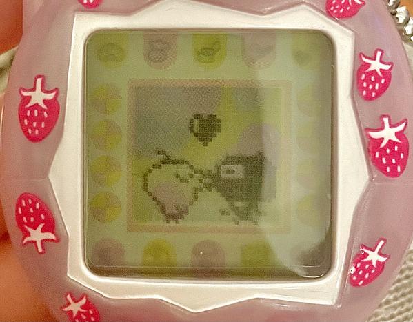 close up photograph of a tamagotchi connection device. on the screen, memetchi and gozarutchi are kissing.