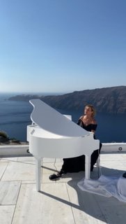 Pianist at a white grand piano on a terrace overlooking the caldera