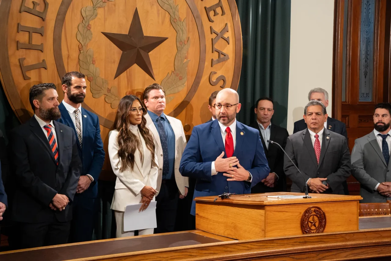 Texas State Representative Cody Harris speaking at a podium in the Texas State Capitol, with supporters standing behind him