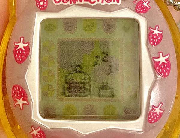 close up image of a tamagotchi connection device. on the screen, memetchi sleeps next to her sleeping baby. they are so small and cute.