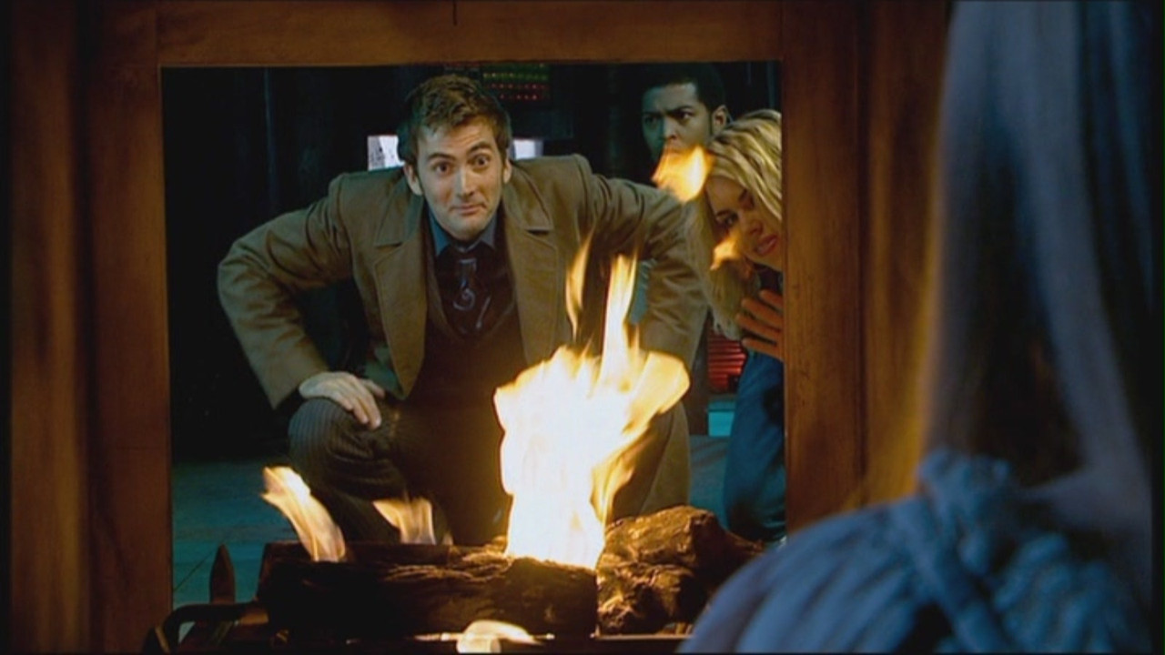 Screencap from The Girl in the Fireplace: from the other side of a fireplace, the Doctor crouches and grins at a girl (obscured by the camera). He's flanked by a smiling Rose and bemused Mickey.